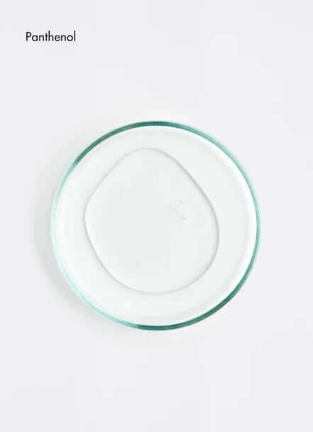Clear gel sample of Panthenol on a glass petri dish, showcasing its smooth texture for skin care applications.