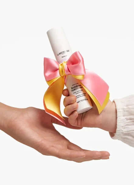Gift of beauty: a hand passing a skincare product adorned with a pink and yellow ribbon, perfect for Mother's Day.