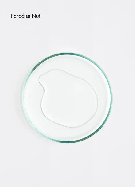 A clear drop of Paradise Nut oil on a round glass dish against a white background.